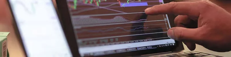 A trader pointing at price charts on a laptop screen